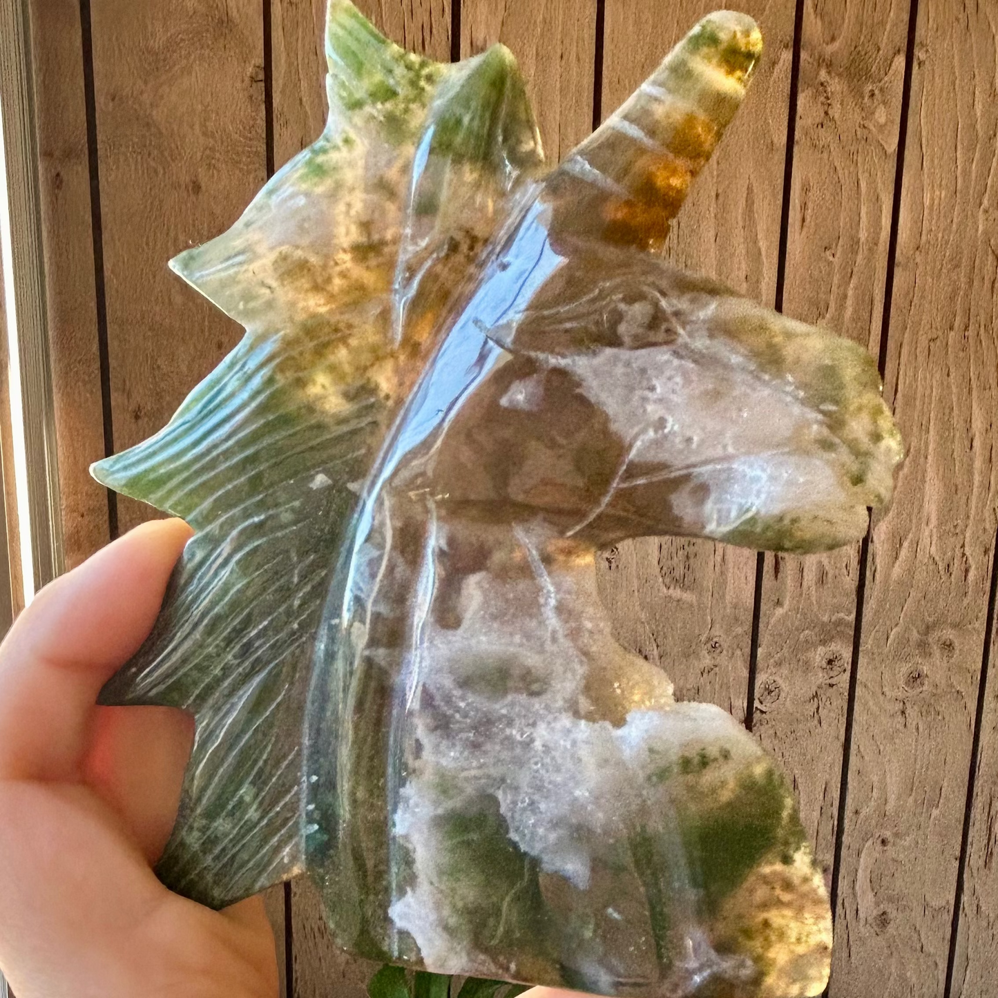 Hand holding a translucent green crystal with a wooden background