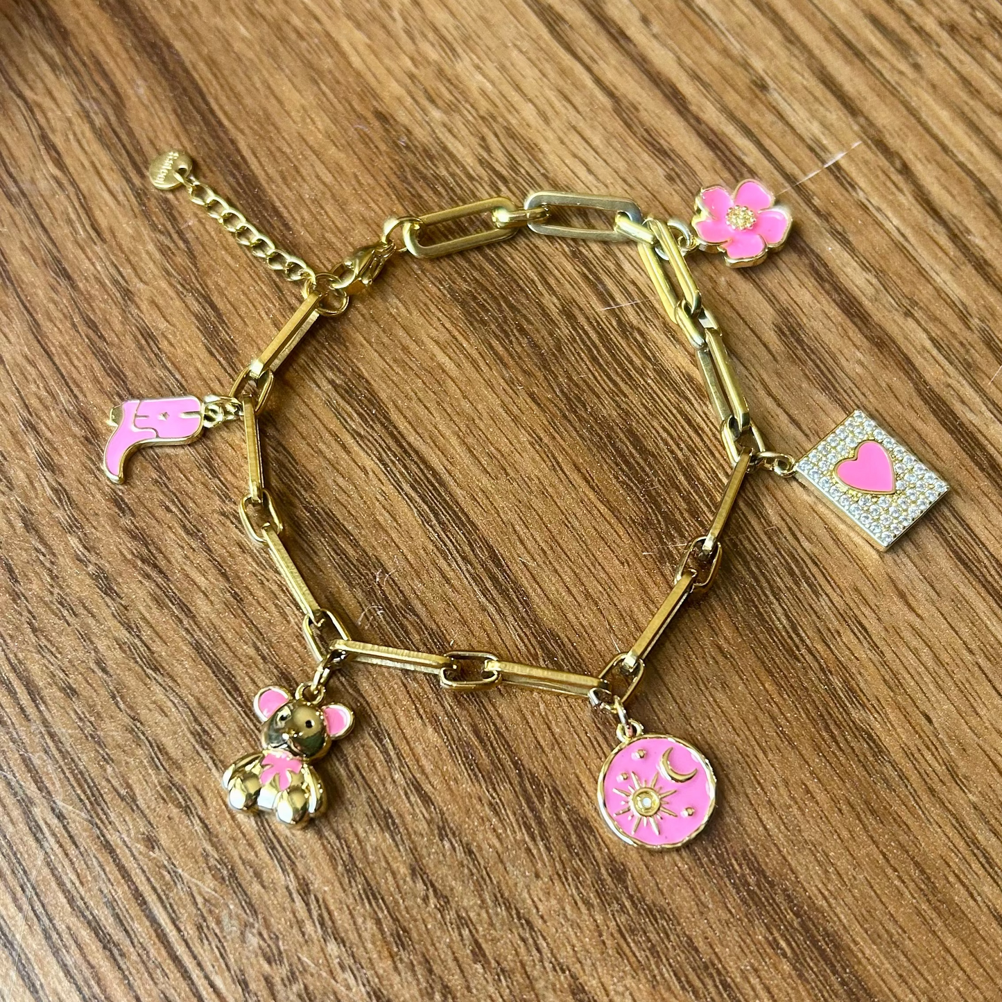 Gold bracelet with pink charms on a wooden surface
