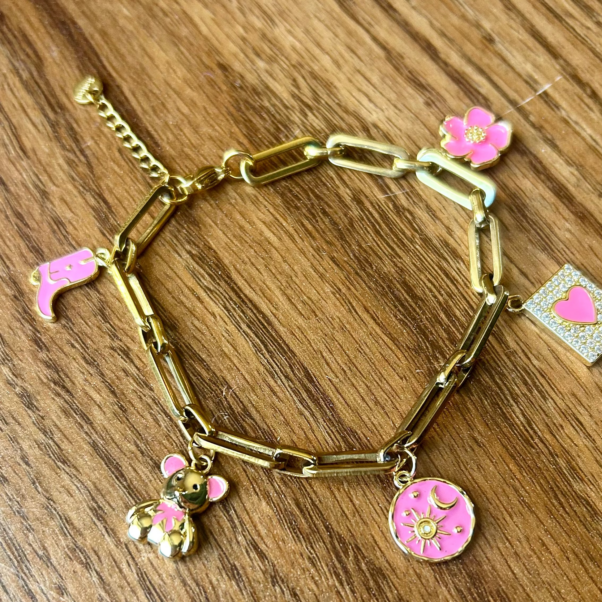 Gold bracelet with pink charms on a wooden surface
