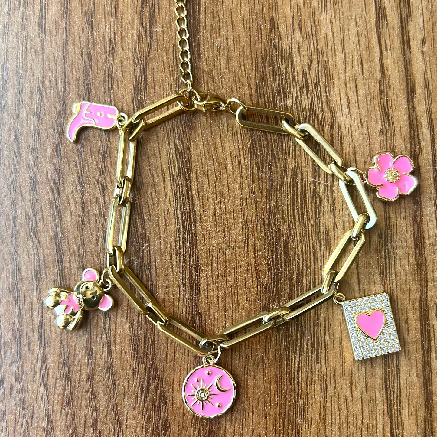 Gold bracelet with pink charms on a wooden surface