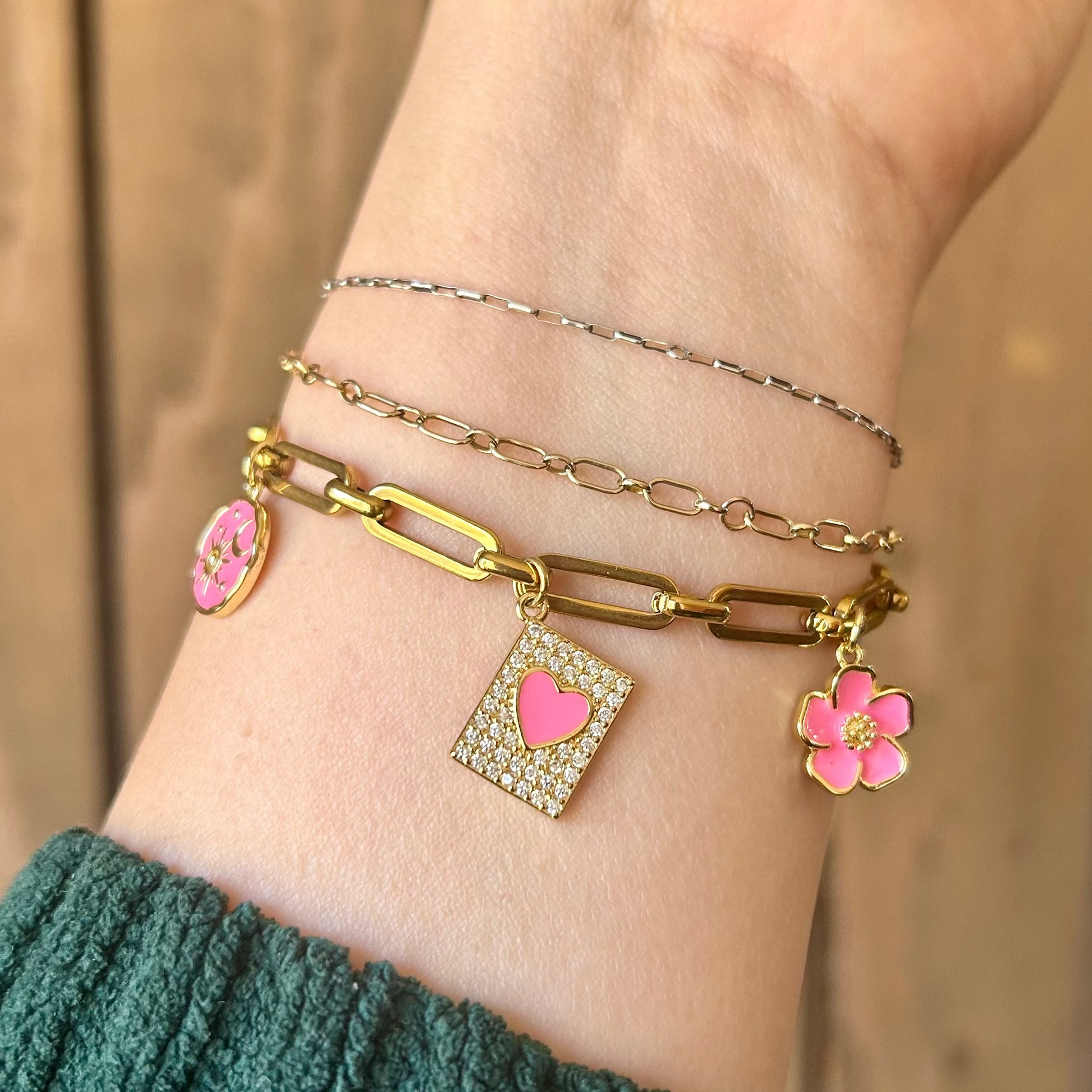 Hand wearing multiple bracelets with floral charms on a wooden background