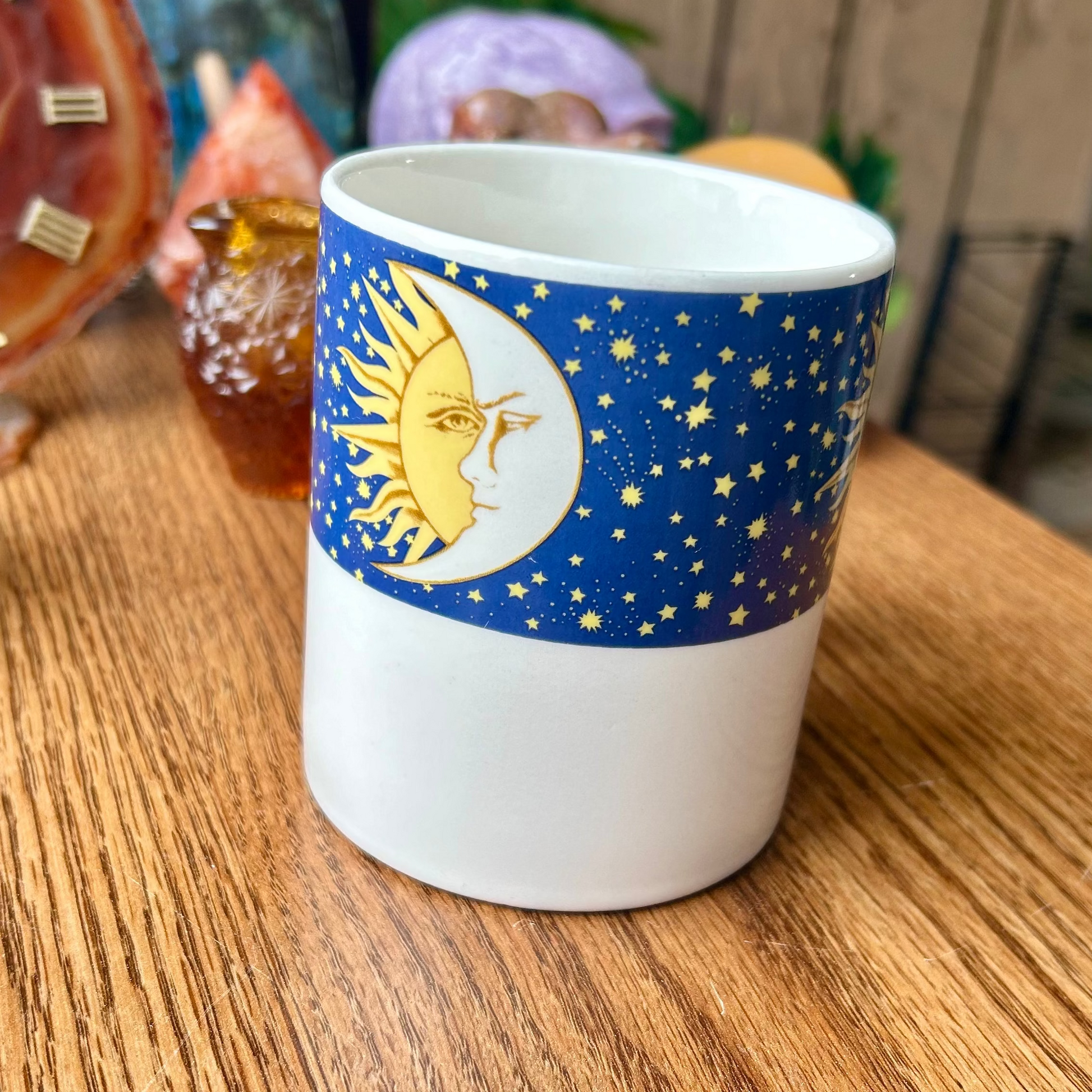White mug with blue sleeve featuring celestial design on a wooden surface