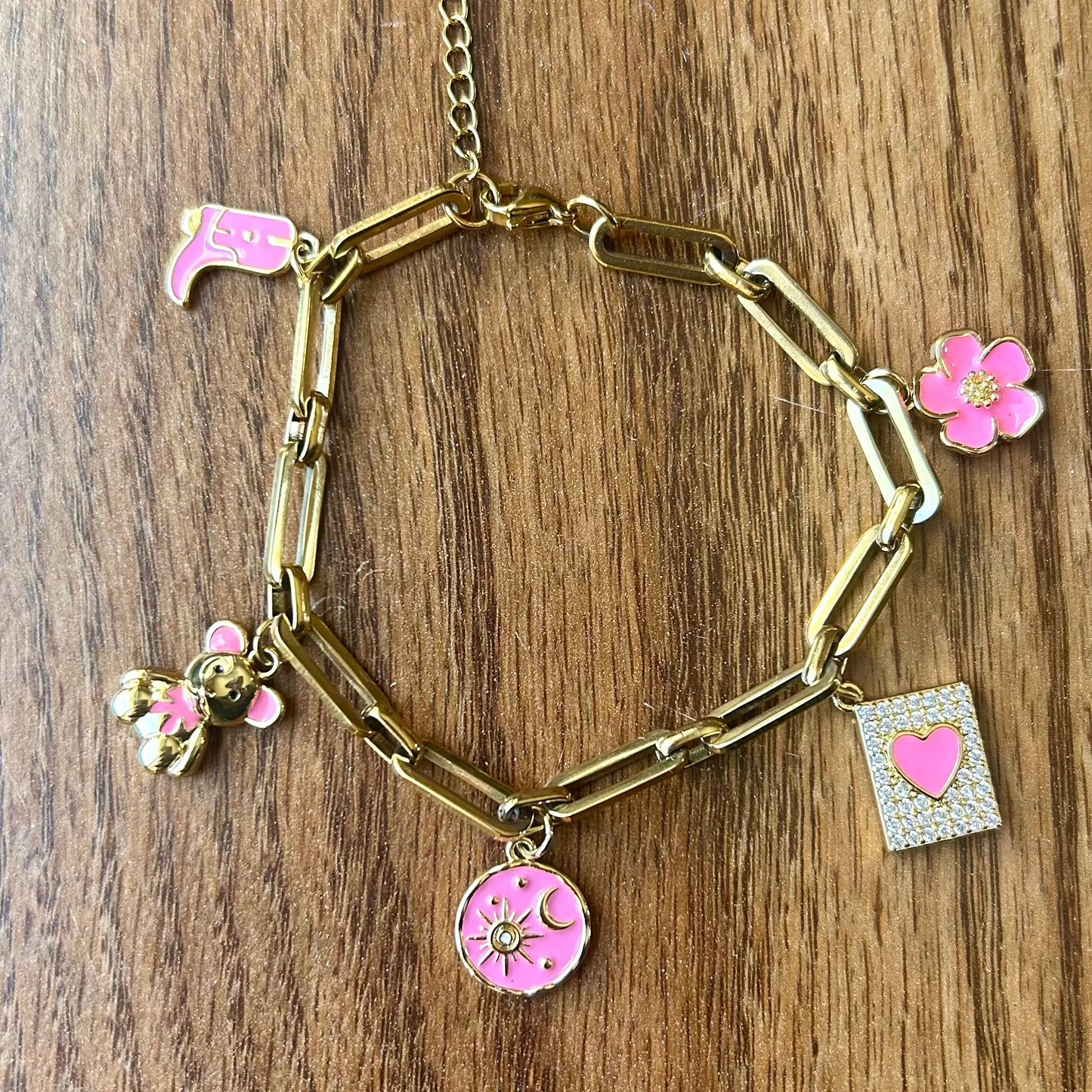 Gold bracelet with pink charms on a wooden surface
