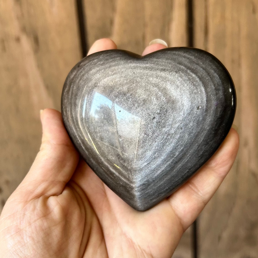 Heart-shaped stone held in a hand against a wooden background