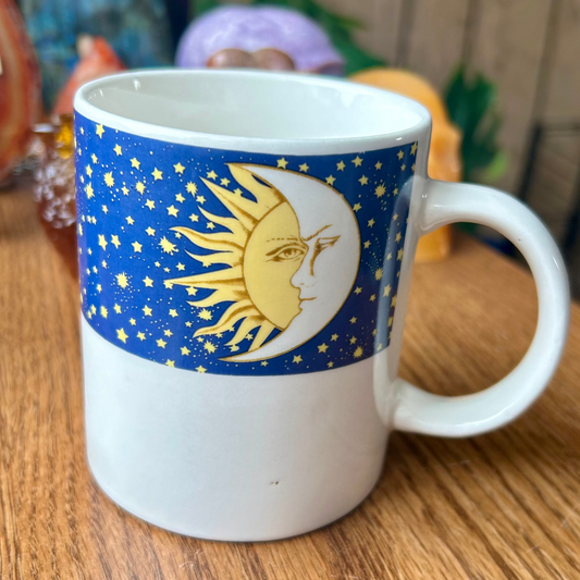 White mug with a blue design featuring a sun and moon on a wooden surface.