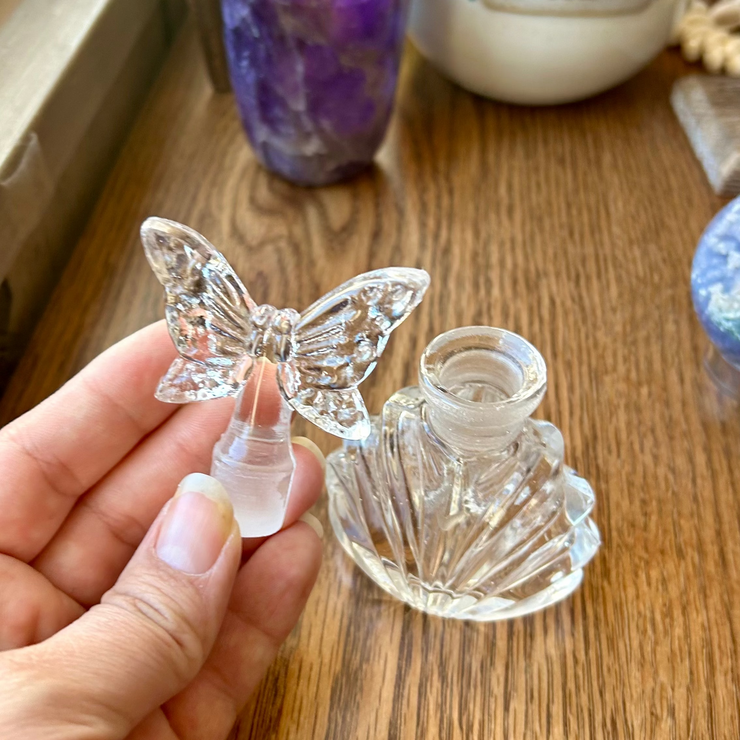 Clear butterfly-shaped object held by a hand on a wooden surface with decorative items in the background.